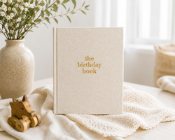 The Birthday Book heirloom keepsake journal with linen cover and gold foil lettering · The Birthday Book open to a birthday memory page with writing prompts · The Birthday Book interior pages showing letter and memory sections · The Birthday Book premium keepsake journal for recording 18 years of birthdays · The Birthday Book linen cover detail with gold accent lettering · The Birthday Book lay-flat binding for easy writing · The Birthday Book archival acid-free pages for lasting memories · The Birthday Boo